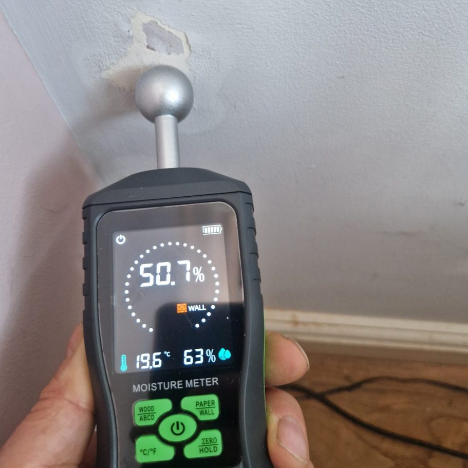 Moisture meter displaying a reading of 50.7 in a wall corner.