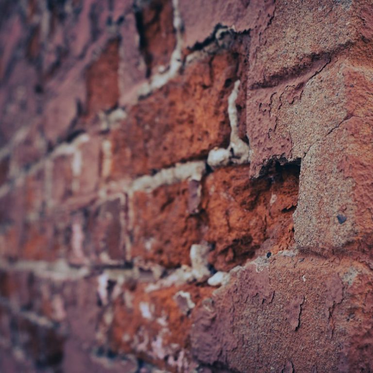 Close-up of a weathered red brick wall with varying textures and hues.